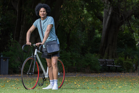 African American man standing on grassy park lawn holding white fixie bicycle with messenger bag