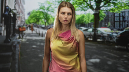 Fototapeta premium Woman standing, bare shoulders visible, wearing draped pink and yellow blouse, facing camera on a city street; quiet contemplation.