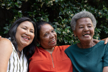 Obraz premium Diverse female friends smiling and leaning in garden by floral vine wall, wearing colorful tops
