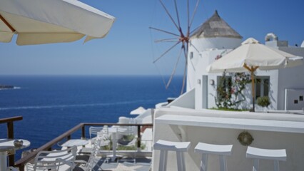 Obraz premium Seaside terrace with white chairs, umbrellas and distant windmill in soft defocused bokeh outdoor background; backdrop copyspace calm.