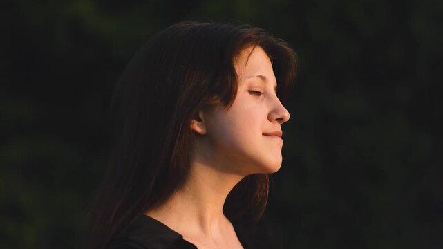 A dreamy portrait of a teenage girl in a lush meadow, turning her gaze toward the golden sun as poplar fluff floats by. Nature, peace, soft light, youth, inspiration, summer, serenity