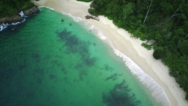 Serene beach scene with turquoise water and lush greenery in Teluk Ijo, Banyuwangi, East Java, Indonesia, featuring a small island and mountainous landscape.