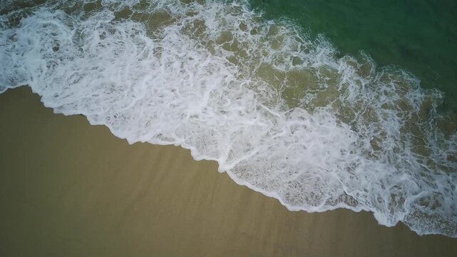 Aerial view of ocean waves gently lapping onto the sandy shore of Teluk Ijo, Banyuwangi, East Java, Indonesia with a serene natural setting.