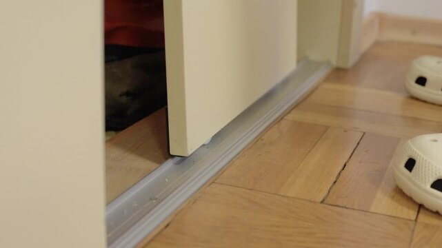 Closeup sliding door bottom track mechanism showing metal guide on parquet floor with roller wheel and sill visible slow motion focus on alignment