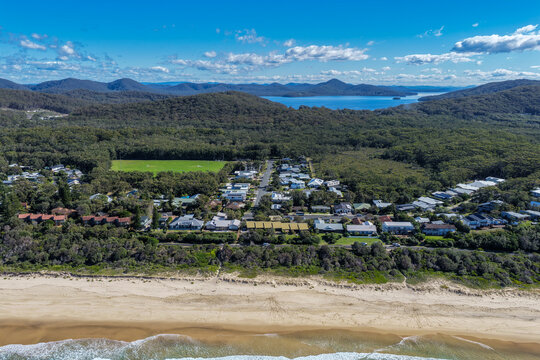Aerial scene capturing Boomerang Beach near Pacific Palms, NSW, Australia, with residential homes and native bushland visible in the background. The sandy shoreline, clear ocean waters and surrounds.
