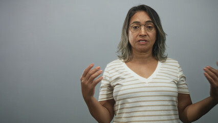 Obraz premium Woman wearing striped v neck shirt and glasses gesturing with open hands and palms while speaking in studio; concern explanation conversation.