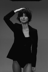 Fototapeta premium Black and white portrait of a confident woman with short hair wearing a black jacket, posing with her hand on her head.