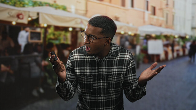 Black man holding a car key fob with an open palm questioning gesture at an outdoor street cafe while pressing the remote; frustration waiting.