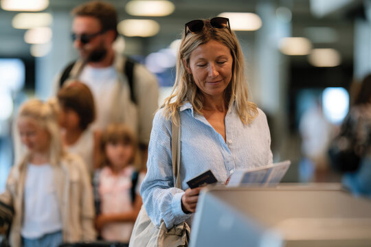 A woman is engaged in checking her tickets while waiting in line at an airport check-in counter, surrounded by travelers of various ages in a busy terminal setting.
