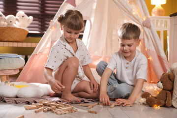Little girl and boy playing with building blocks in wigwam at home © New Africa