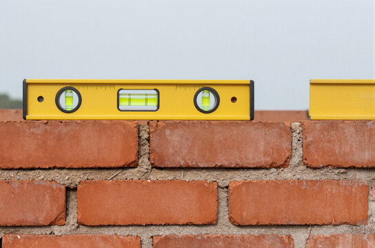 yellow spirit level on red brick wall under construction with clear sky in background