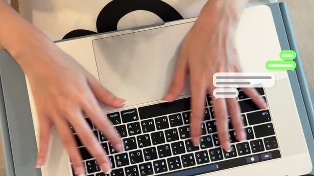 Top view 4K shot of an East Asian woman's hands typing on a laptop keyboard with green chat balloons popping up on the right side.