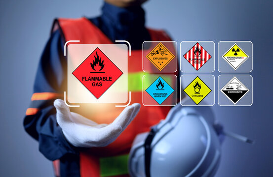 An industrial worker holds floating hazardous material placards, representing hazmat classification, dangerous goods transportation safety, and industrial safety compliance