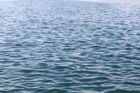 Aerial close-up view of calm ocean or sea water surface showing natural blue-green ripple texture with soft light reflection