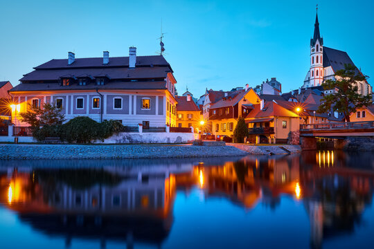 Czech Krumlov, Czech Republic. Evening view at bridge in old town with old houses and broach at tower of St. Vitus Church. Sunset blue hour with evening illumination.
