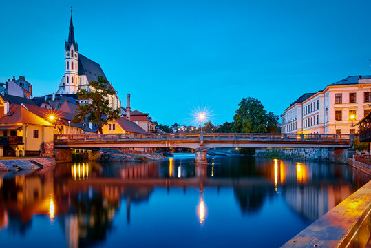 Panoramic view of Czech Krumlov, Czech Republic. Evening view at bridge in old town with old houses and broach at tower of St. Vitus Church. Sunset blue hour with evening illumination.