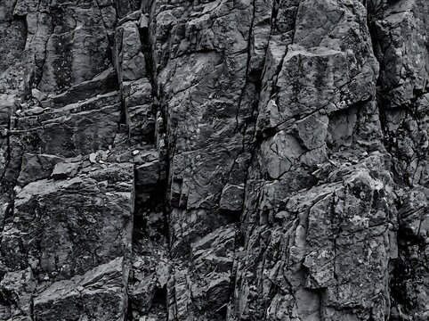 Dark rugged rocky cliff face with deep crevices and cracks