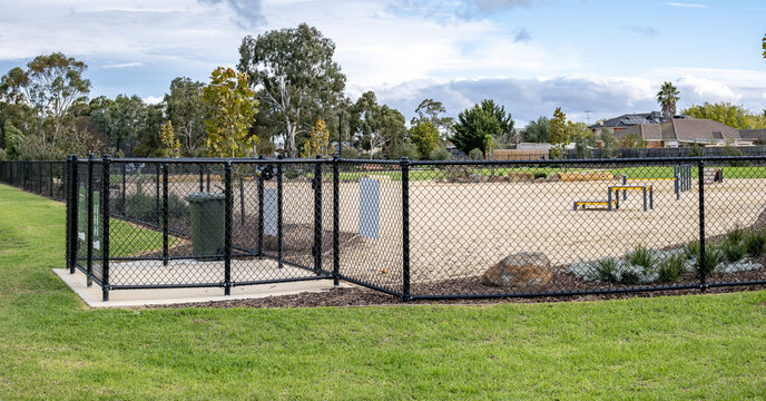 A fenced off-leash dog park with a double-gated airlock entry system in a suburban public park in Melbourne, Australia. Chain-link enclosure features two sequential gates forming a secure buffer zone