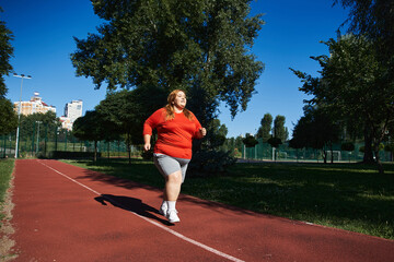 Fototapeta premium Curvy woman embraces fitness through outdoor running in sunny park