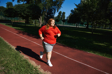 Obraz premium Empowering plus size woman enjoys outdoor running in vibrant park setting under blue skies