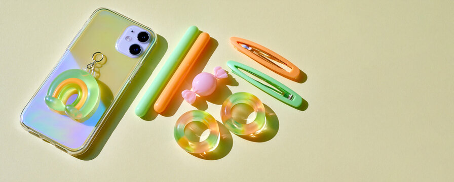 Jelly aesthetic smartphone accessories with pastel translucent charms hair clips and candy colored rings arranged in bright sunlight on minimalist background