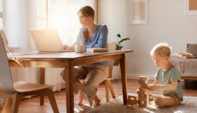 Mother Working on Laptop at Home While Young Son Plays with Wooden Blocks on Bright Sunny Day in Cozy Living Room Space