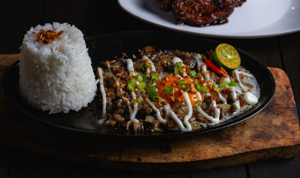 close up photo of spicy sizzling sisig pork mask meal with fried rice, egg and mayonaise on top on a sizzling plate.