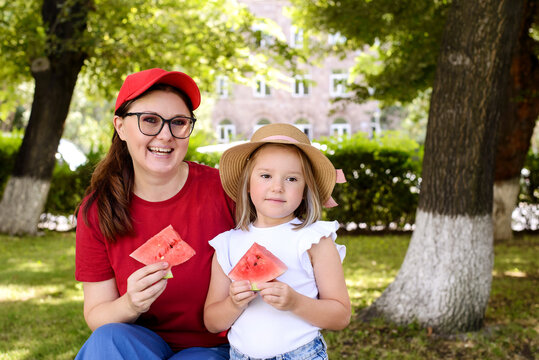 Mother and daughter holding watermelon slices in a sunny park. Happy family bonding, healthy summer snack, outdoor lifestyle, childhood memories, and wholesome recreation concept