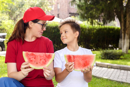 Mother and son holding watermelon slices and sharing a warm moment in a sunny park. Healthy family lifestyle, summer refreshment, outdoor bonding, and childhood happiness concept