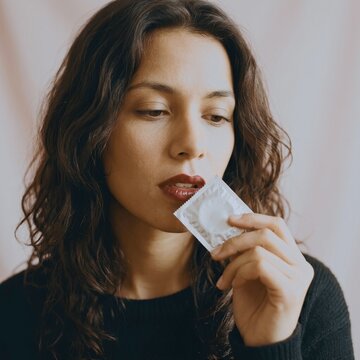 Woman with dark hair holding condom wrapper close up indoors