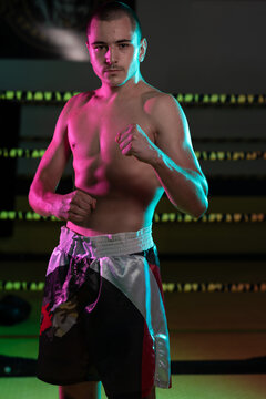 Young Male Boxer In Fighting Stance Training In Boxing Ring With Neon Lighting Portrait