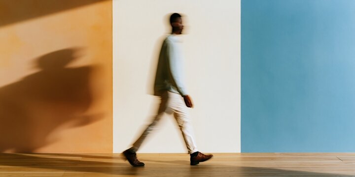 Motion blur of a man walking past a colorful wall with copy space, his blurred figure moving across a vibrant yellow and blue background for business concepts