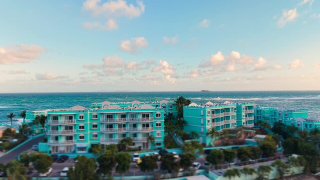 Drone view of a luxury tropical resort with bright blue buildings on Saint Martin island in the Caribbean Sea. Aerial look at beautiful seaside apartments and multi story accommodation complex.