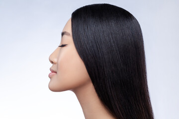 Profile portrait of gentle beautiful Asian young woman with long smooth straight dark hair and closed eyes looking peaceful and relaxed isolated on gray background © khosrork