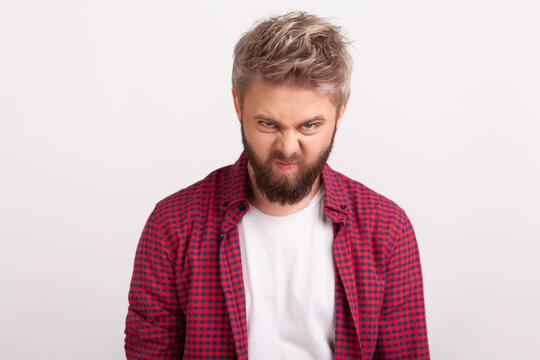 Angry bearded man looking aggressively at camera with deeply squinted eyes furrows on forehead posing isolated over white background