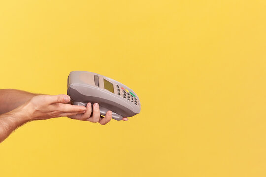 Anonymous worker holding payment terminal for contactless checkout to process secure bank transaction or mobile purchase using nfc technology isolated over yellow background with copy space