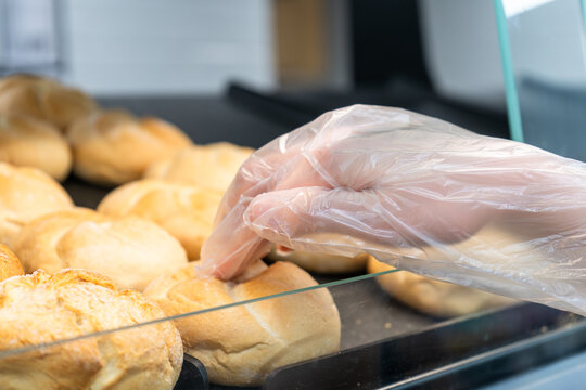 Customer selecting fresh bread roll with disposable glove at self service bakery display