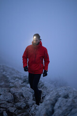 Balancing on the Mountain Trail at Dusk.A lone hiker balances on a rocky mountain trail during early morning or dusk, with a headlamp lighting the misty path. © .shock