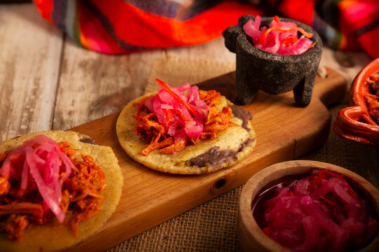 Panuchos Mexican Food, a typical dish from Yucatan, Mexico. A handmade, fried corn tortilla filled with beans, topped with cochinita pibil, pickled red onion, and habanero pepper.
