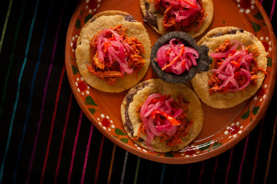 Panuchos Mexican Food, a typical dish from Yucatan, Mexico. A handmade, fried corn tortilla filled with beans, topped with cochinita pibil, pickled red onion, and habanero pepper.