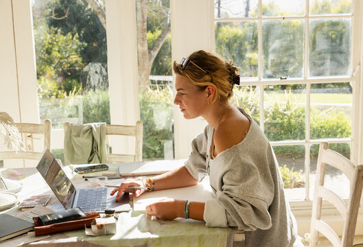 young woman artist in her studio using laptop and working on a pencil drawing