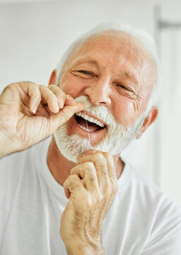Portrait of an elderly senior man is cleaning brushing his teeth using dental floss in front of mirror in bathroom. Dental hygiene, vitality and beauty concepts