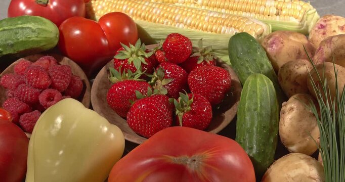 Hand takes strawberries from a wooden plate. Close-up footage of  corn, strawberries, cucumbers, tomatoes, green onions, potatoes, raspberries, dill, sweet peppers on a rotating table.