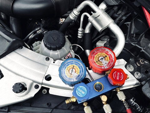 car air conditioning system inspection with manifold gauge set connected inside engine bay show automotive AC pressure testing refrigerant service maintenance and repair diagnostic process professiona
