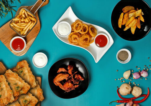 Top View Assorted Cafe Snacks,  french fries, onion rings, chicken wings, appetizer, tempe mendoan, and Finger Foods on Turquoise Background