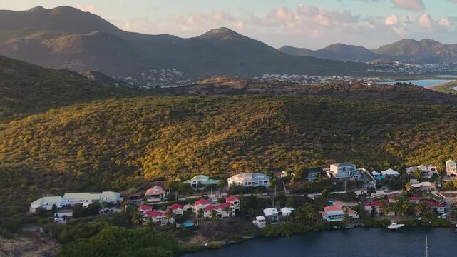 Drone aerial view of Oyster Pond bay on the border of Sint Maarten and Saint Martin. Tropical island landscape features luxury coastal houses and boats anchored in the calm harbor.