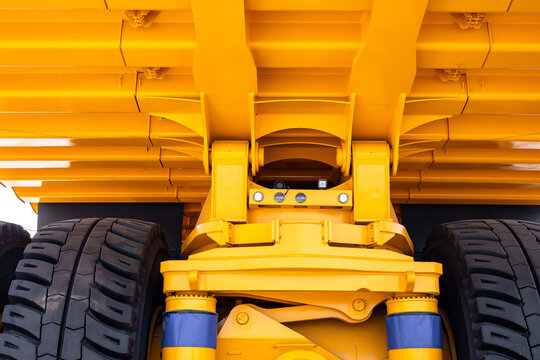 Low-angle close-up of the undercarriage of a heavy-duty yellow dump truck focusing on suspension components, hydraulic cylinders, chassis beams and twin rear