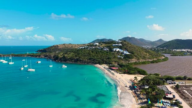 Aerial view of Friar's Bay and Etang Guichard salt pond on the French side of Saint Martin island in the Caribbean. White sand beach organized with beach umbrellas, sunbeds, and people relaxing.