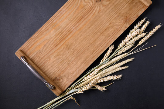 wooden tray board and sheaf of ears of grain on a black stone table top view.