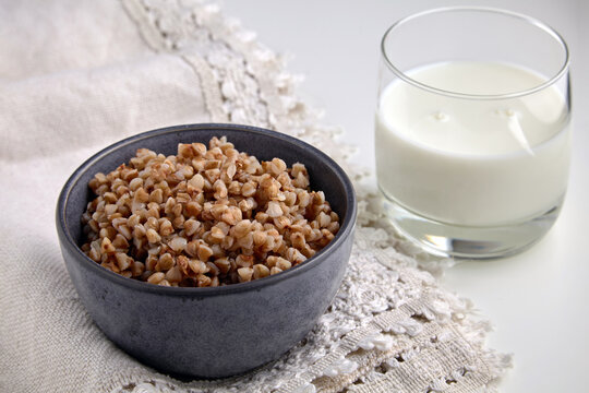boiled buckwheat in a ceramic bowl and a glass of milk on a linen tablecloth.